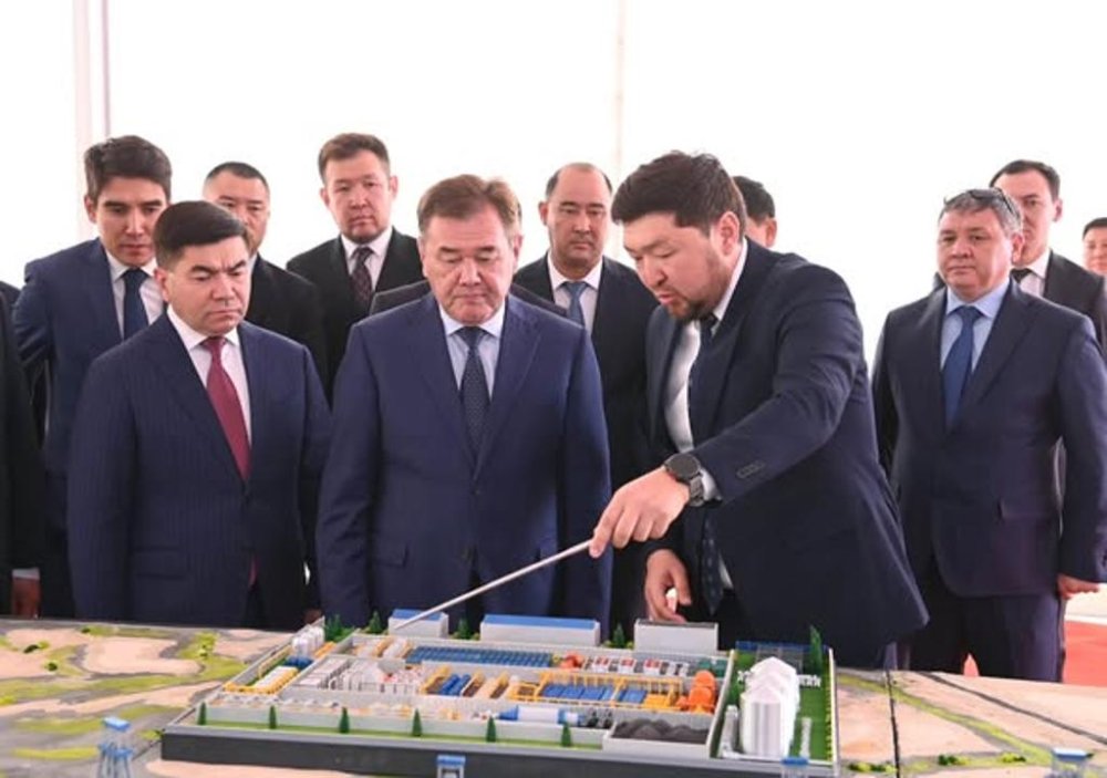 Жаңақорған ауданында тау-кен байыту комбинатының құрылысы басталды 11-ден 1 слайд. Костюм киген ерлер тобы өндірістік нысанның макетін қарап тұр.